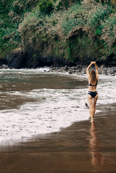 Girl in bikini with her back  walking on black beach. - Photo, image