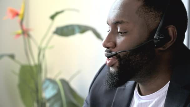 Впевнений афроамериканець, дружній бородатий чоловік у навушниках, експерт, працівник кол-центру або оператор підтримки, розмовляє з клієнтом, проводить віддалену онлайн-консультацію, посміхається дружньо - Кадри, відео