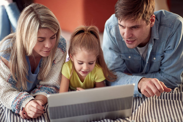 Mom and Dad teaching their little daughter in a relaxed atmosphere at home how to use a computer. Family, home, togethernes - Фото, зображення