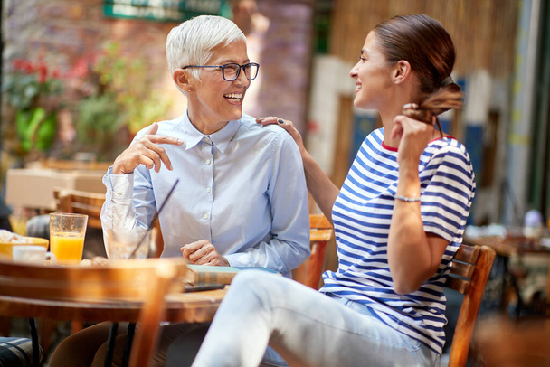 Two female friends of different generations have a friendly talk while they have a drink in a pleasant atmosphere in the bar. Leisure, bar, friendship, outdoor - Foto, immagini