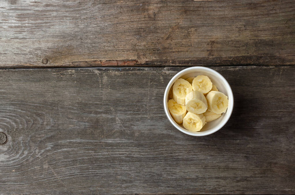 Rebanadas de plátanos en un plato blanco sobre un fondo rústico de madera preparándose para cocinar con espacio para copiar. - Foto, imagen
