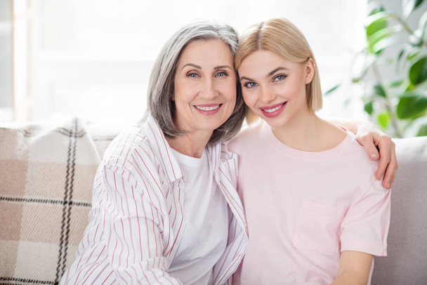 Photo of lovely sweet happy mother and daughter good mood hug sit couch indoors inside house home apartment - Foto, afbeelding