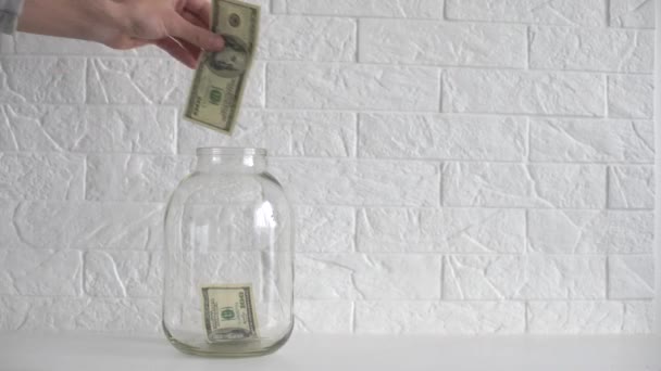 käsi laittaa dollarin setelin säästöpurkkiin valkoisella etiketillä - Materiaali, video