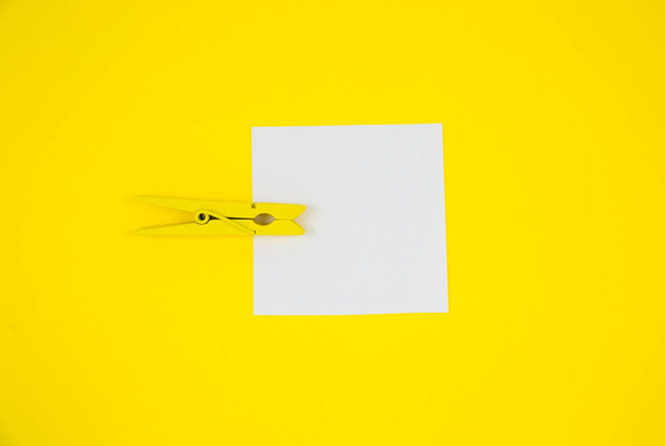 空白黄色の木製の布ピンでリストステッカーを行うには.黄色の背景にメモ用紙を閉じます。コピースペース。ミニマリズム、オリジナルで創造的な写真. - 写真・画像