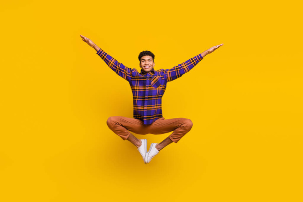 Full length body size photo of young man smiling childish careless jumping up isolated vibrant yellow color background - 写真・画像