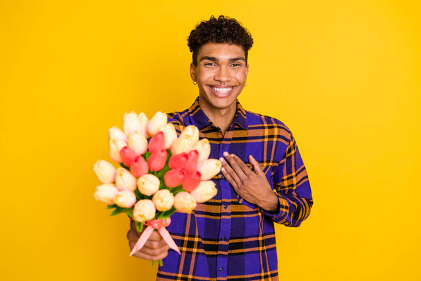 Photo portrait of cheerful man keeping hand on chest giving tulips bouquet isolated on vivid yellow color background - Fotografie, Obrázek
