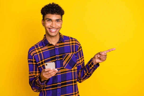 Portrait photo de l'homme gardant téléphone portable montrant l'espace vide doigt sourire isolé sur fond de couleur jaune vif - Photo, image