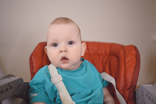 Pequeño niño divertido recién nacido emocional sentado en la silla alta de alimentación. Expresiones faciales del bebé y plantilla de embalaje de mercancías. Niño sano, concepto de hospital y maternidad feliz. Bebé.. - Foto, imagen