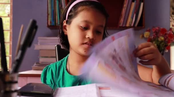 Una niña india linda estudiando y leyendo libros teléfono inteligente en la mesa - Metraje, vídeo