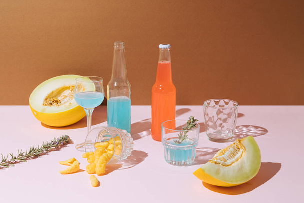 Verano, escena de fiesta con dos botellas de cócteles, melones, vasos y aperitivos sobre fondo rosa, marrón.. - Foto, imagen