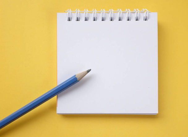 flacher Bleistift auf weißem Spiralblock auf gelbem Hintergrund - Foto, Bild