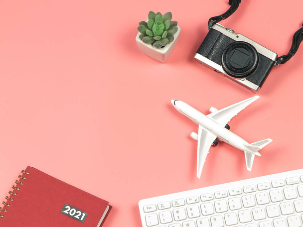 Top view or flat lay of airplane model, computer keyboard, camera, red 2021 diary and cactus on pink background, business and traveling concept. - Photo, image
