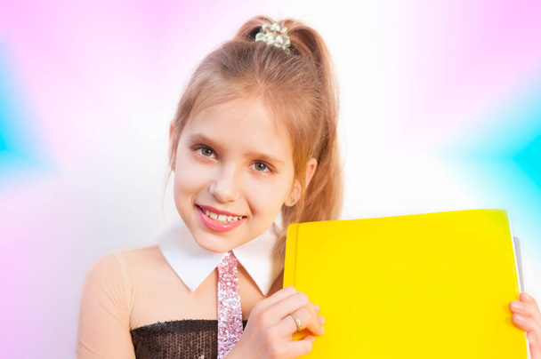 A girl with a business folder in her hands smiles at the pink, ultra violet background. She smiles, she has a beautiful smile. A teen girl is dressed in a business suit with a pink tie - Foto, afbeelding
