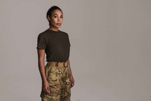 Confident african american soldier woman posing and looking at camera isolated over grey wall - Фото, изображение