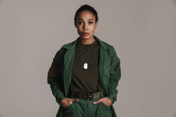 Confident african american soldier woman posing with hands in her pockets isolated over grey wall - Photo, Image