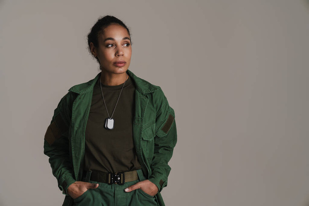 Confident african american soldier woman posing with hands in her pockets isolated over grey wall - Foto, afbeelding