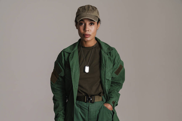 Confident african american soldier woman posing with hand in her pocket isolated over grey wall - Foto, afbeelding