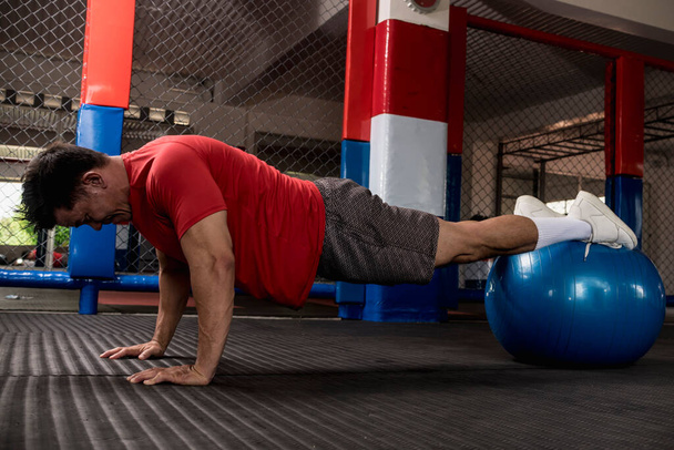 Um homem asiático musculoso e apto faz flexões em uma bola de estabilidade. Exercício e treino abdominal e central. Disparo aéreo. - Foto, Imagem
