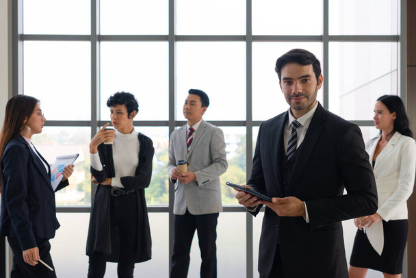 портрет молодого кавказского уверенного бизнесмена с улыбающимся лицом, стоящим у власти на фоне многонациональных коллег. разнообразие в концепции бизнеса - Фото, изображение