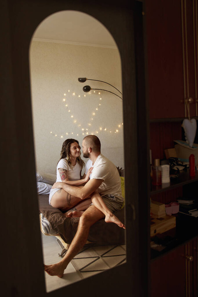 Couple are cuddling indoors on the bed at home and looking into each other - 写真・画像