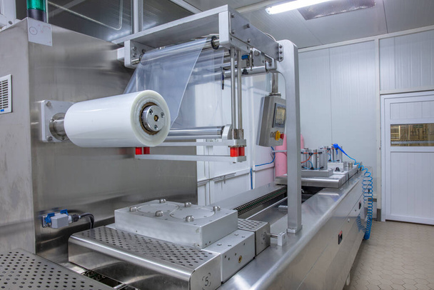 Procesamiento de envasado de mantequilla y queso en la máquina de sellado de envasado al vacío de alimentos en la fábrica industrial de alimentos. Embalaje de mantequilla de alimentos y queso en línea de producción. Máquina de vacío. - Foto, imagen