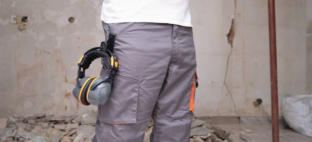 Costruttore irriconoscibile con protezione dell'udito appeso ai pantaloni. Concetto di sicurezza sul lavoro. - Foto, immagini