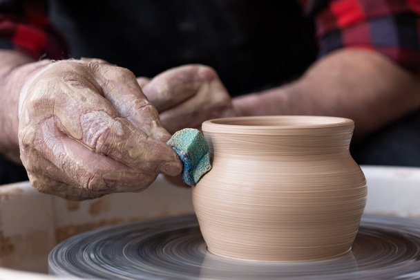 Mannelijke handen reinigen met spons aardewerk op een pottenbakkerswiel. - Foto, afbeelding