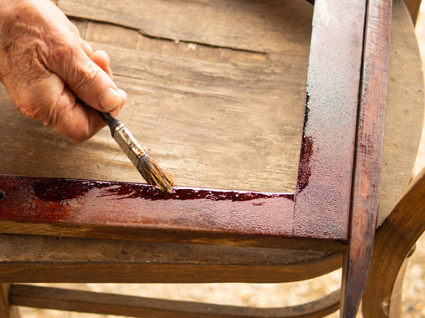 An elderly man restores old furniture and paints a wooden chair with varnish. The paint brush glides over the wooden surface. - Photo, Image