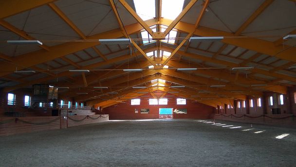 Foto de uma sala de equitação interior vazia para cavalos e cavaleiros. A escola de equitação é adequada para curativos e pular cavalos durante todo o dia - Foto, Imagem