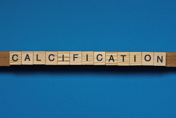gray word calcification in small square wooden letters with black font on a blue background - Foto, immagini