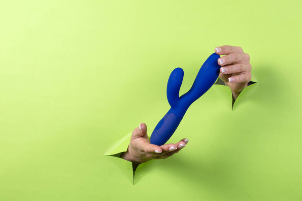 Erotic toy for pleasure in the hands of a woman on a green background. A device for masturbating a woman. Blue dildo for women - Zdjęcie, obraz