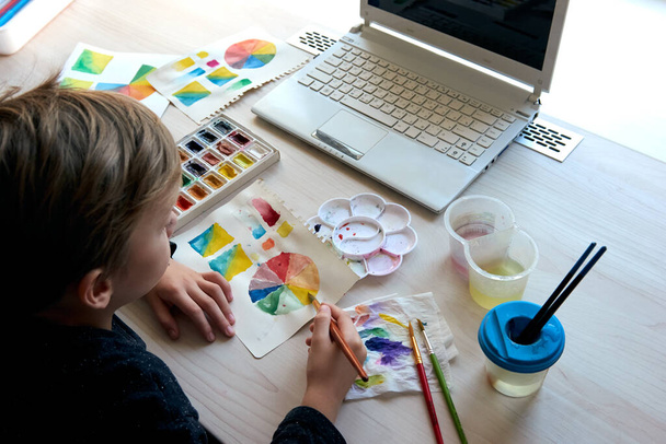 Jongen schilderen foto 's met aquarelverf verf tijdens kunstles online - Foto, afbeelding