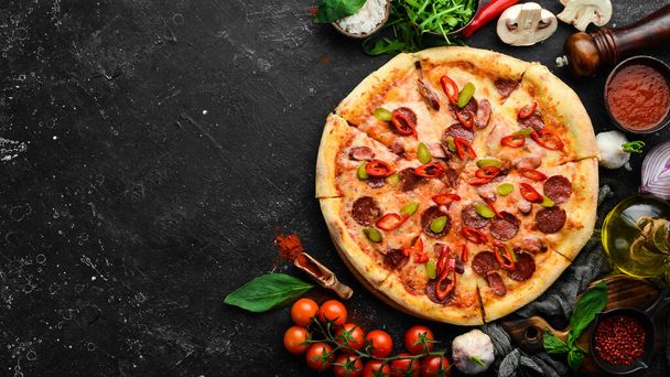 Spicy pizza with sausages and chili peppers. On a black stone background. Free space for text. - Photo, Image