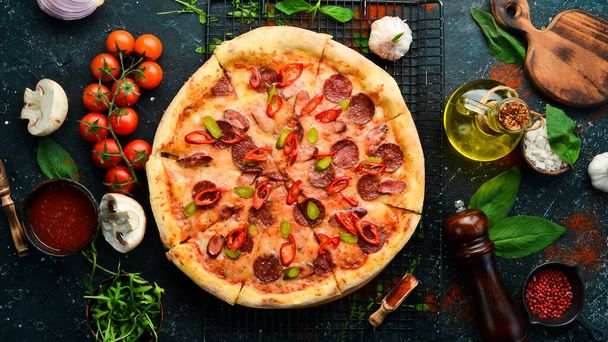Spicy pizza with sausages and chili peppers. On a black stone background. Free space for text. - 写真・画像