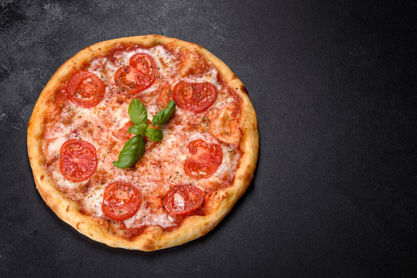 Gustosa pizza fresca al forno con pomodori e formaggio su uno sfondo di cemento scuro - Foto, immagini