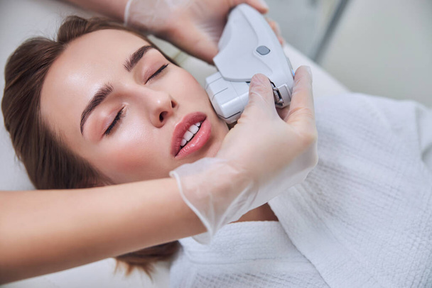 Charming attractive Caucasian woman getting process rejuvenation on modern device in beauty salon - Foto, immagini