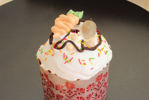 Свежеприготовленные пасхальные торты в бумажных формах, украшенные помадкой, шоколадной глазурью и сахарными яйцами и морковью - Фото, изображение