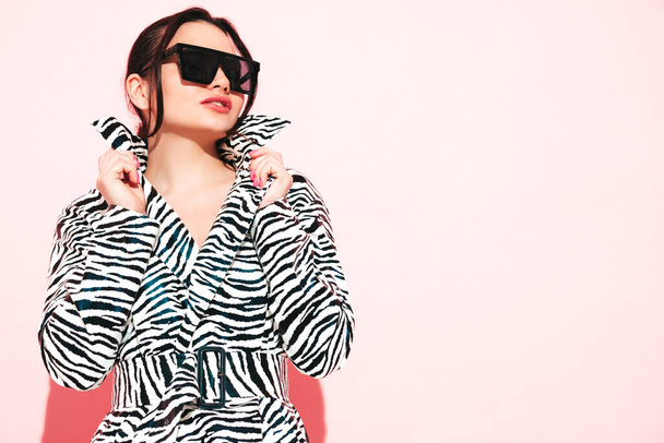 High fashion portrait of young beautiful brunette woman wearing nice trendy summer zebra coat.Sexy fashion model posing near pink wall in studio.Fashionable female in sunglasses - Φωτογραφία, εικόνα