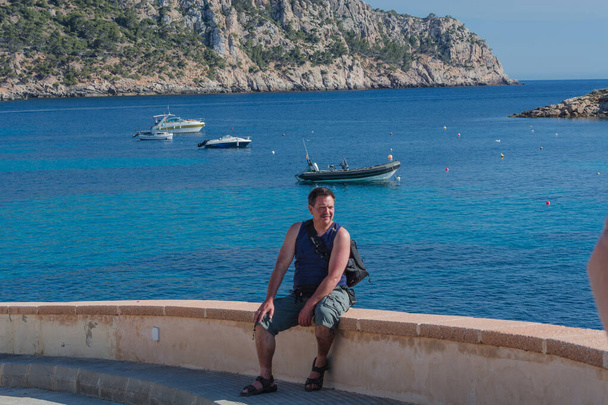 Hombre sentado en una pared con vistas al lado del mar y relajante - Foto, Imagen