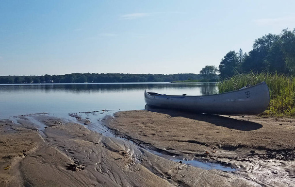 ビーチでの空のカヌーと穏やかな昼間の湖のシーン - 写真・画像