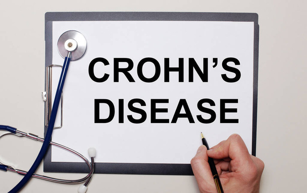 On a light background, a stethoscope and a sheet of paper, on which a man writes CROHN IS DISEASE. Medical concept - Photo, image