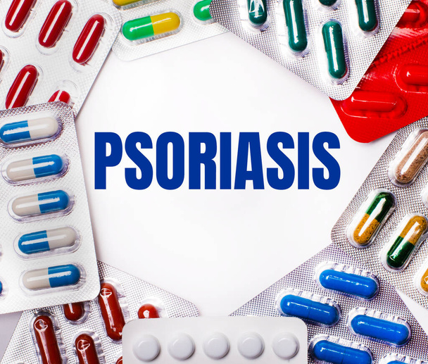 The word PSORIASIS is written on a light background surrounded by multi-colored packages with pills. Medical concept - Фото, изображение