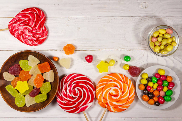 Барвисті шоколадні цукерки, льодяники та желе на білому дерев'яному столі
 - Фото, зображення