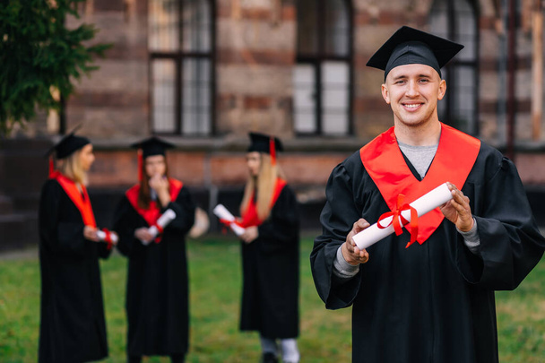 szczęśliwy student w stroju akademickim i kapelusz posiada certyfikat uniwersytecki lub akademii. Koncepcja absolwenta. - Zdjęcie, obraz