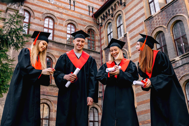 Счастливые студенты в холостяцких одеждах и с дипломами на открытом воздухе после церемонии. - Фото, изображение
