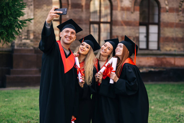 groep gelukkige afgestudeerden studenten gebruiken mobiele telefoon om selfie samen te nemen. Na ontvangst van diploma 's. - Foto, afbeelding