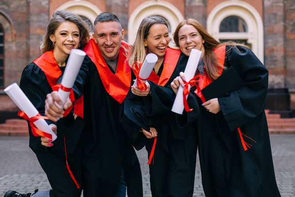 Estudantes de graduação em chapéu e vestido, ao ar livre, mostrando um certificado de graduação da universidade. - Foto, Imagem