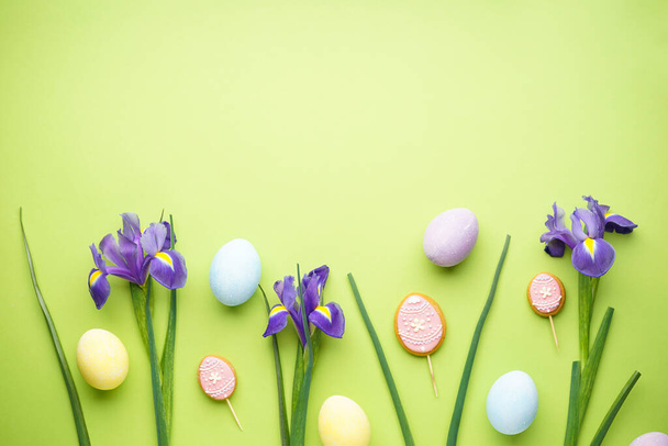 Easter eggs and irises flowers on light green background, space for text, top view - Foto, Imagen