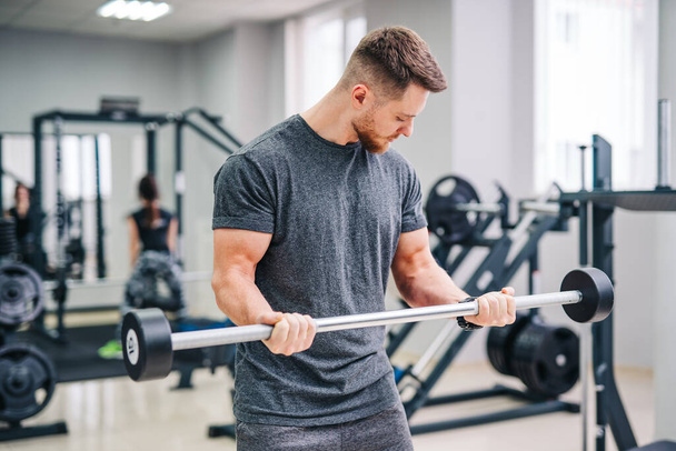 Athletic physical man training in the fitness gym. Strong handsome male working with sport equipment. - Fotoğraf, Görsel