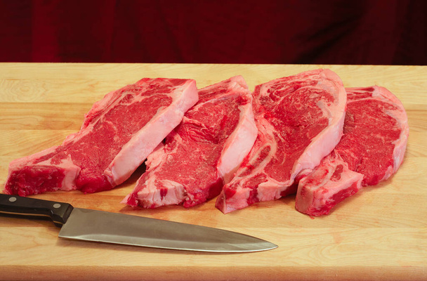 Vier steaks op een snijplank, met slagersmes - Foto, afbeelding